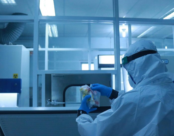 Lab technician in full protective suit performs tasks in a controlled laboratory environment.